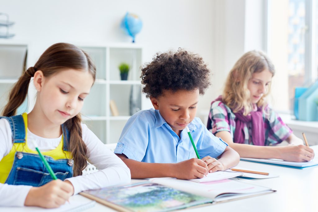 Três crianças escrevendo em sala de aula
